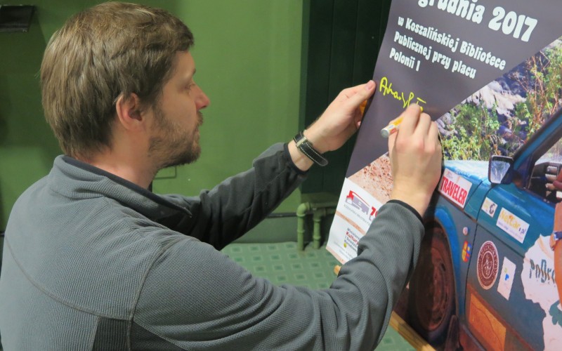 Arkady Paweł Fiedler składa podpis na plakacie promującym spotkanie