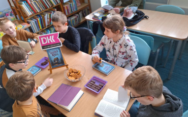 dzieci siedzą przy stole z bibliotekarką i dyskutują o przeczytanej książce