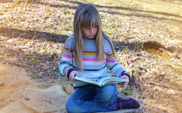 Dziewczynka czyta książkę siedząc na ziemi