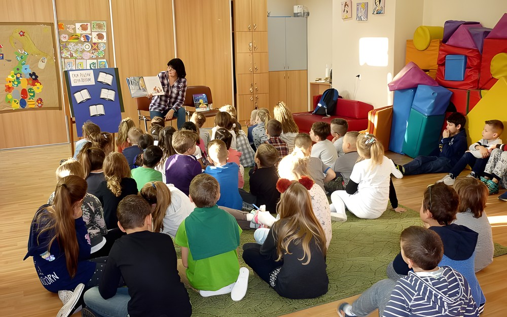 Dzieci siedzą na dywanie i słuchają czytanej przez Panią Wiolę książki "Paddington"
