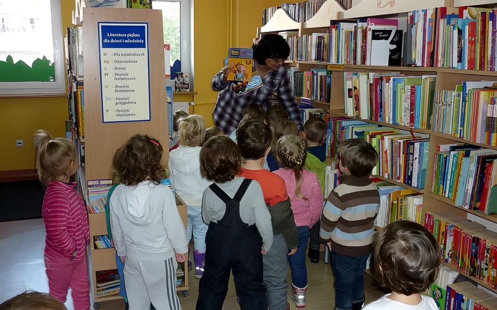 Pani Wiola pokazuje dzieciom, gdzie znajdą w bibliotece książeczki dla siebie