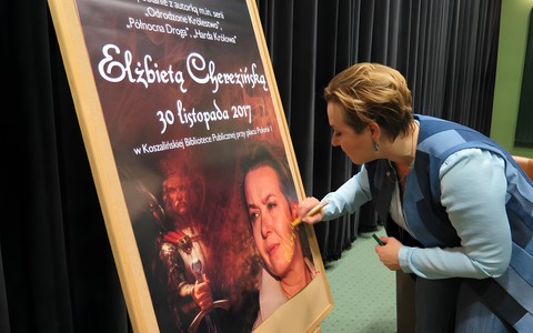 Elżbieta Cherezińska podpisuje plakat promujący spotkanie autorskie w Koszalińskiej Bibliotece Publicznej