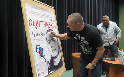 Łukasz Orbitowski składa pamiątkowy autograf na plakacie promującym spotkanie