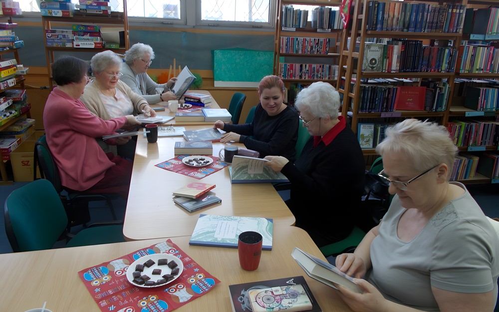 Panie siedzą przy stole i dyskutują z bibliotekarką o książce