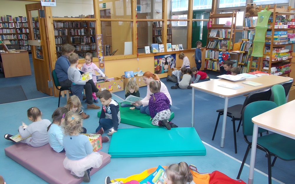 Dzieci wraz z nauczycielkami i bibliotekarką oglądaja książki