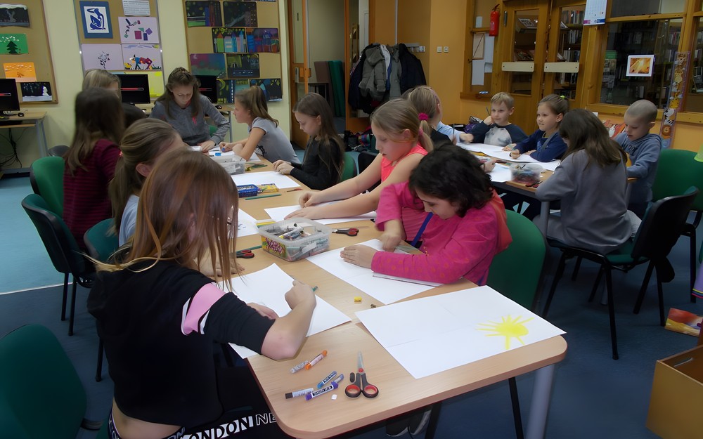 Dzieci siedzą przy stołach  i tworzą prace plastyczne