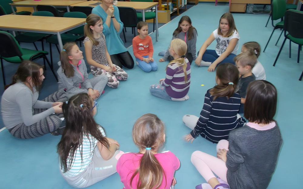 Dzieci z bibliotekarką siedzą w kole podczas wspólnej zabawy