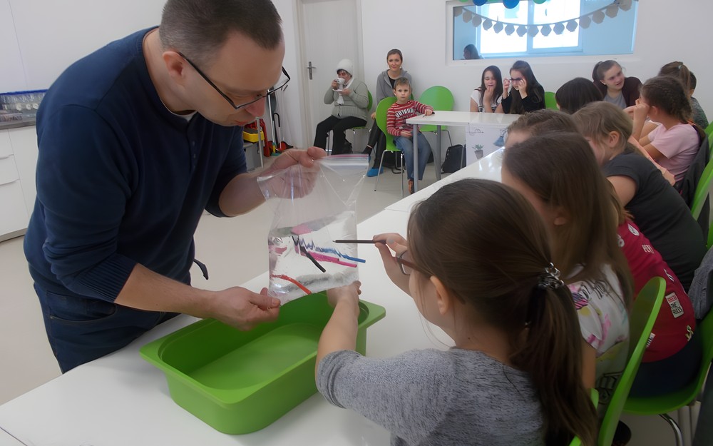 Dziewczynka wbija kredkę w worek napełniony wodą, pozostałe dzieci obserwują co się wydarzy