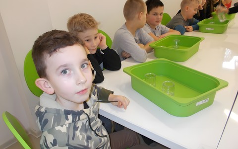 Dzieci siedzą przy stole i wykonują doświadczenia z wodą