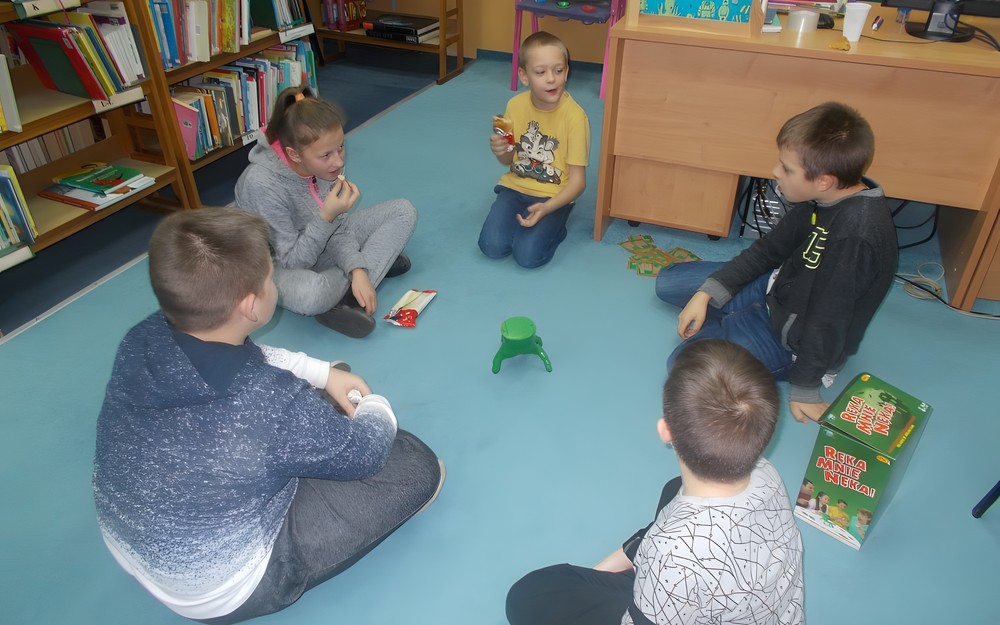 Czworo dzieci siedzi na dywanie i gra w "Ręka mnie nie nęka"