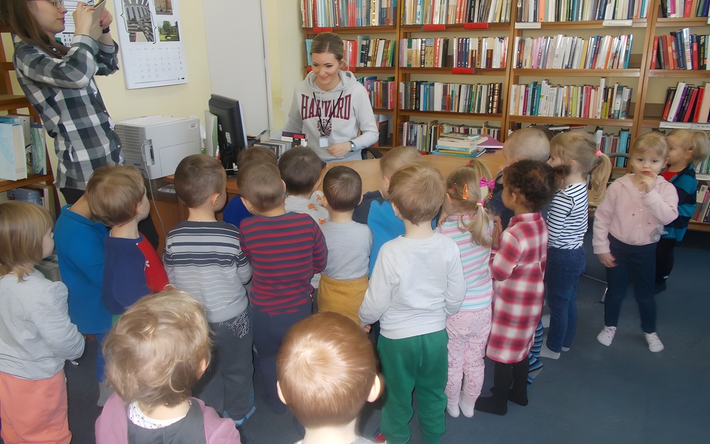 dzieci stoją przy biurku bibliotekarki i obserwują, jak oddaje się książkę