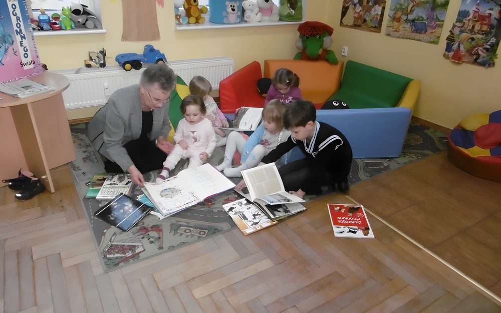 Dzieci wraz z bibliotekarką oglądają ksiażki