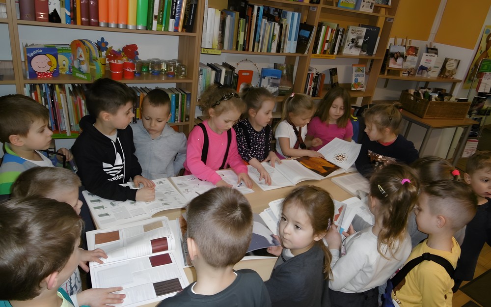 Dzieci przeglądają przygotowane propozycje książkowe dotyczące szydełkowania, haftowania i robienia na drutach.