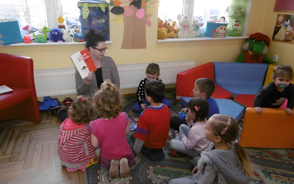 Bibliotekarka prezentuje dzieciom książki dostepne do wypożyczenia.