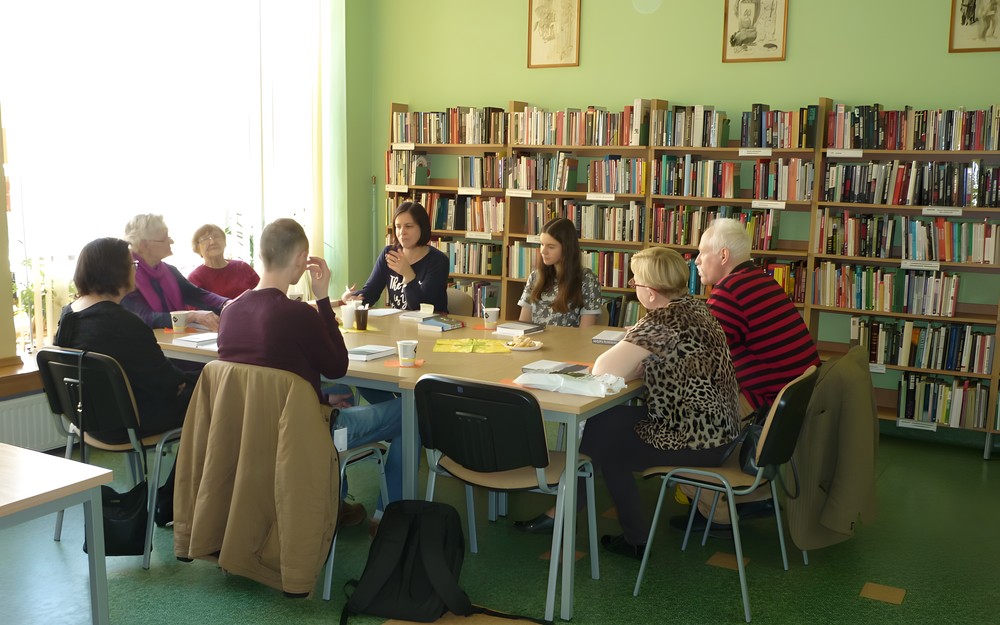 Uczestnicy spotkania siedzą przy stole i rozmawiają o książce