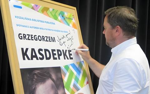 Grzegorz Kasdepke składa pamiątkowy autograf na plakacie reklamującym spotkanie