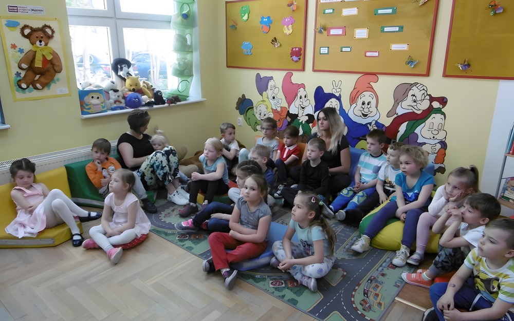 Dzieci siedzą na dywanie i słuchają bajki.