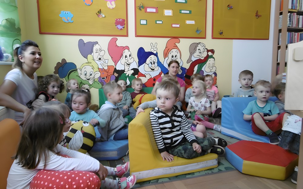 Dzieci siedzą na dywanie i słuchają bajki.