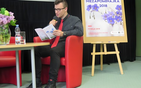 Wychowanek koszalińskiego Pałacu Młodzieży siedzi na czerwonym fotelu przy stoliku i recytuje wiersz