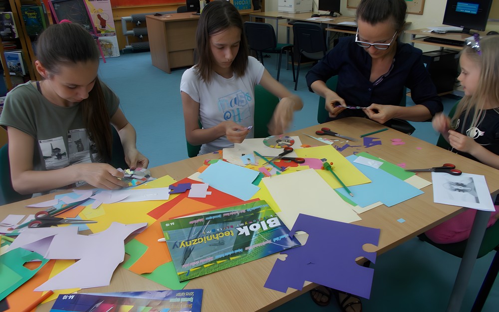 Dzieci wraz z rodziciem siedzą przy stole i wykonują swoje zegary