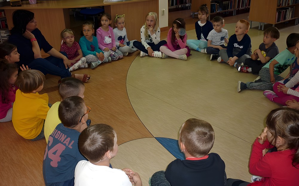 Dzieci i bibliotekarka siedzą w kręgu (po turecku) i rozmawiają o przyjaźni