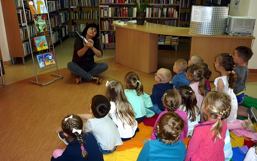 Bibliotekarka pokazuje dzieciom - siedzącym na chuście integracyjnej - książeczki interaktywne