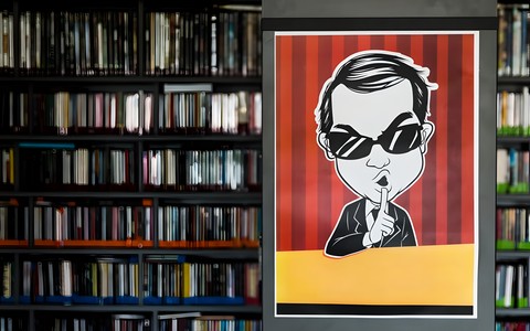 Źródło zdjęcia: pixabay.com. Obraz podzielony na pół. Z lewej strony widnieją regały z książkami. Po prawej stronie jest męźczyzna w okularach przeciwsłonecznych, z palcem na ustach.