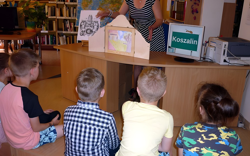 Dzieci siedzą na ławeczkach i słuchają LEGENDY O PIĘKNEJ LINIE (w teatrzyku Kamishibai)