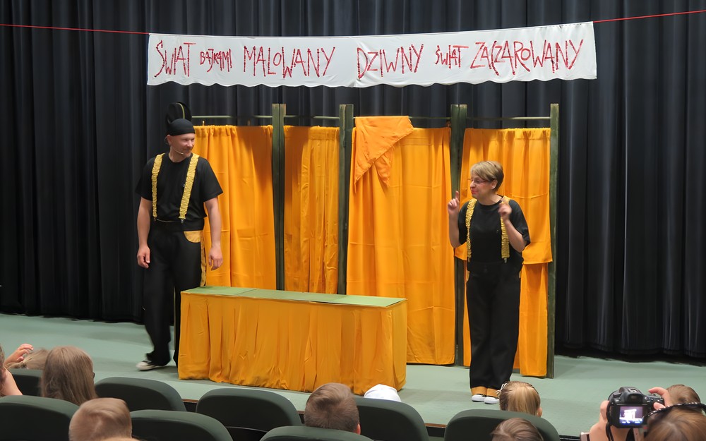 Aktorzy Teatru Władca Lalek ze Słupska (kobieta i mężczyzna) witają wyróżnionych najlepszych czytelników dziecięcych. Na scenie widnieje napis: Świat bajkami malowany. Dziwny świat zaczarowany. Przed sceną, na pierwczym planie widać publiczność