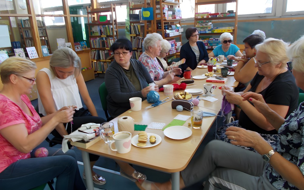 Panie siedzą przy stole i rozmawiają o sztuce rękodzielniczej