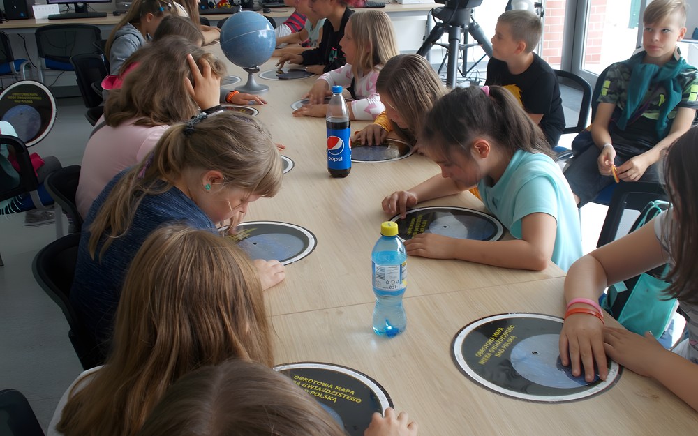 Dzieci siedzą przy stole w obserwatorium i wyszukują swoje znaki zodiaku