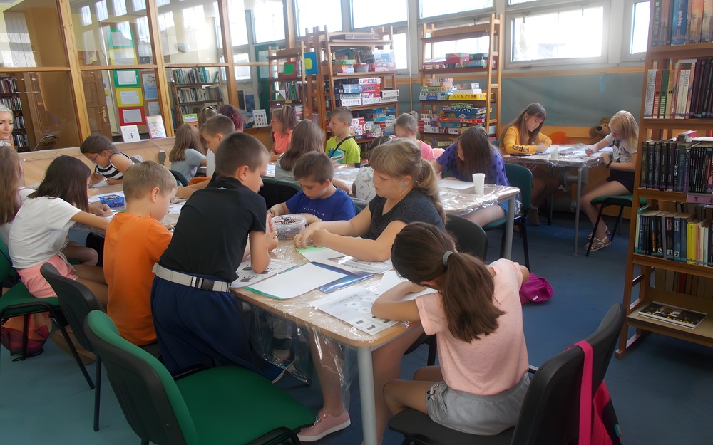 Dzieci siedzą przy stole podczas wykonywania pracy plastycznej