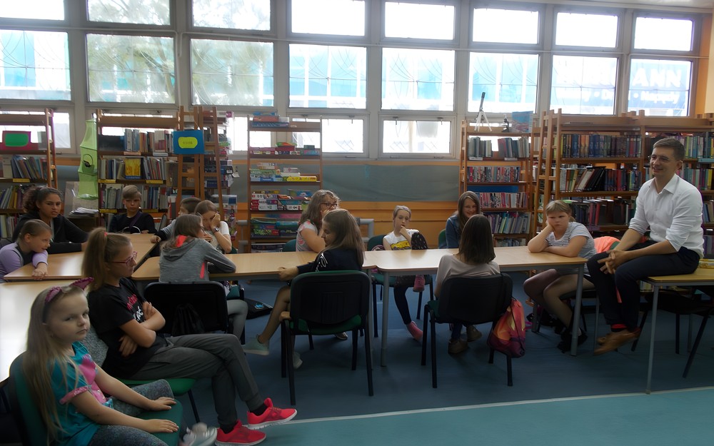 Dzieci siedzą przy stołach słuchając opowieści pisarza