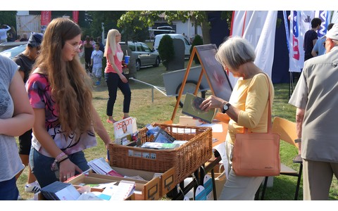 Bibliotekarz przy stoisku promocyjnym Koszalińskiej Biblioteki Publicznej na festynie „Postaw na rodzinę” 2018. Przy stoisku stoi starsza pani i ogląda książki z bookcrossingu.