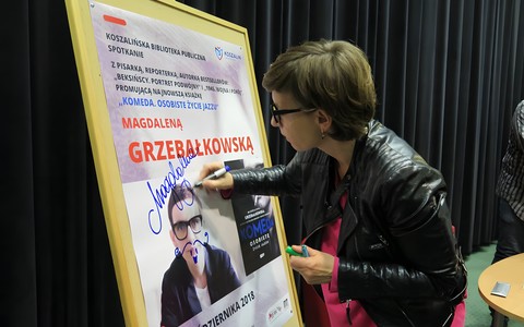 Magdalena Grzebałkowska składa pamiątkowy autograf na plakacie promującym spotkanie w Koszalińskiej Bibliotece Publicznej