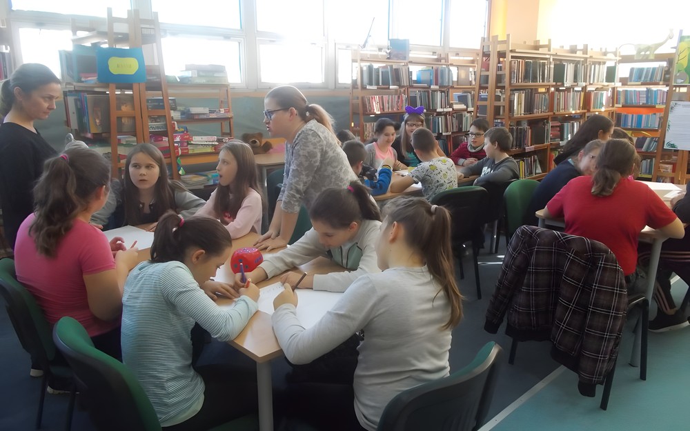 Uczniowie siedzą przy stołach i pracują w grupach