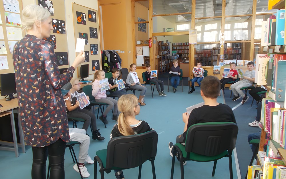 Dzieci siedza w kole trzymając ilustracje ze znanych bajek