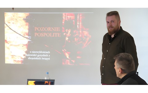 Michał Gierke podczas swojego wykładu „Pozornie pospolite – o niezwykłościach malowideł gotyckich z chojeńskich świątyń”. Po lewej stronie widoczna prezentacja multimedialna na ten temat.