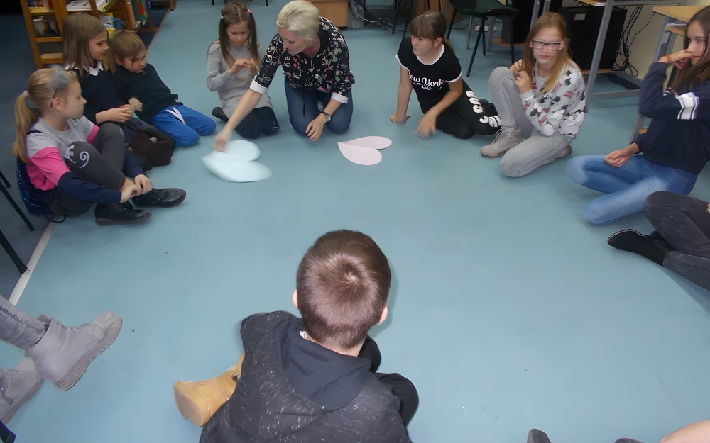 Dzieci siedzą w kole na dywanie podczas wpolnej zabawy z bibliotekarką