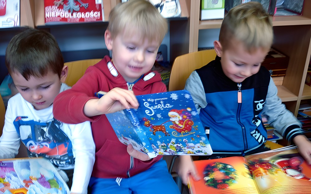 Przedszkolaki siedzą na krzesełkach i przeglądają świąteczne książeczki