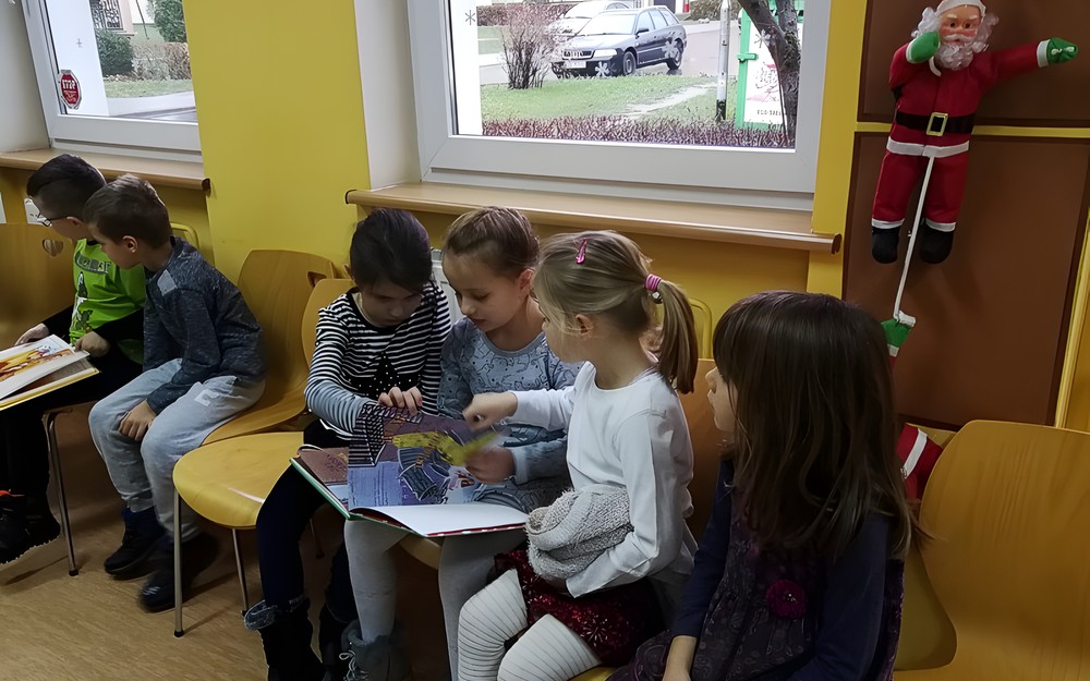 Dzieci siedzą na krzesełkach i przeglądają książeczki o tematyce świątecznej