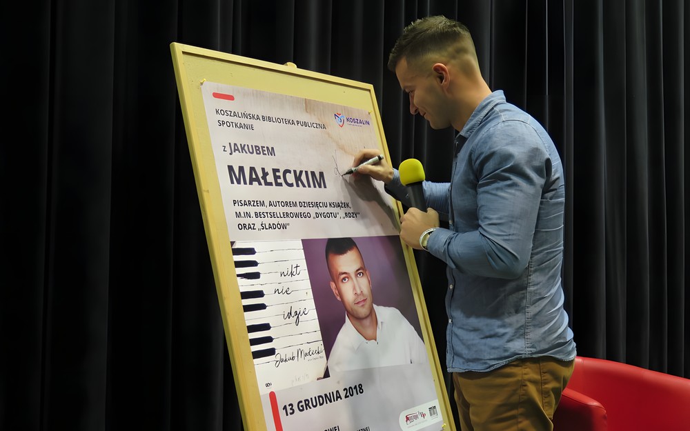 Jakub Małecki składa pamiątkowy autograf podczas spotkania w Koszalińskiej Bibliotece Publicznej