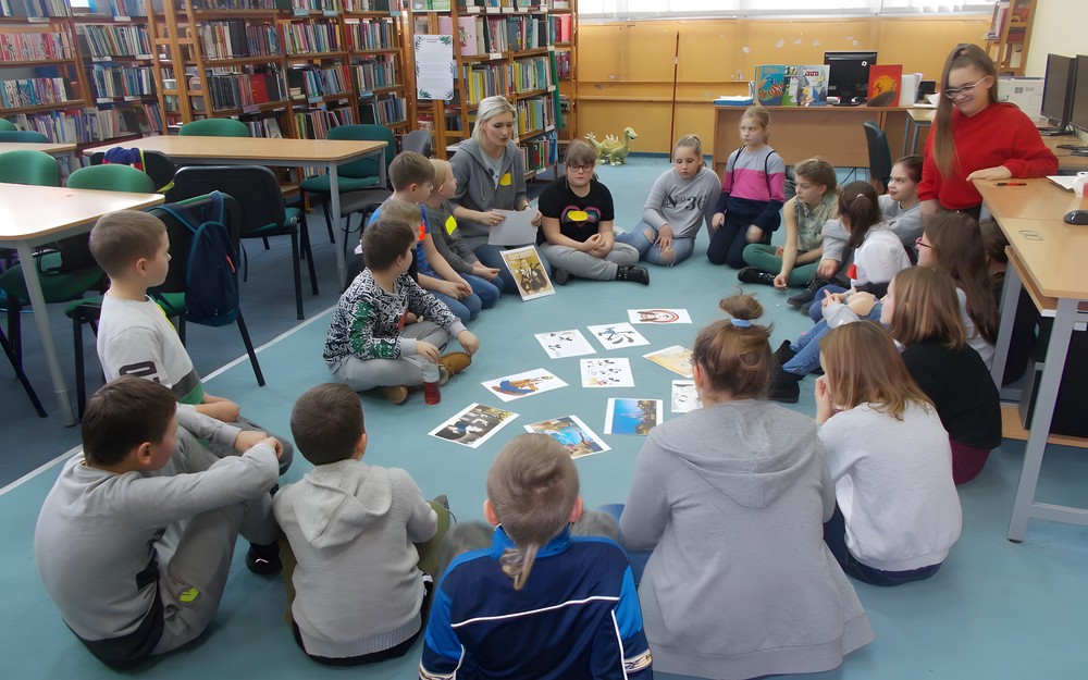 Dzieci siedzą w kole słuchając bibliotekarki opowiadającej o życiu i twórczości Walta Disneya