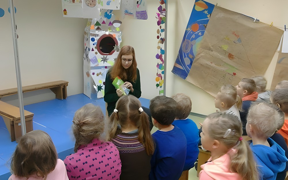grupa przedszkolaków słucha czytanej przez bibliotekarkę książki