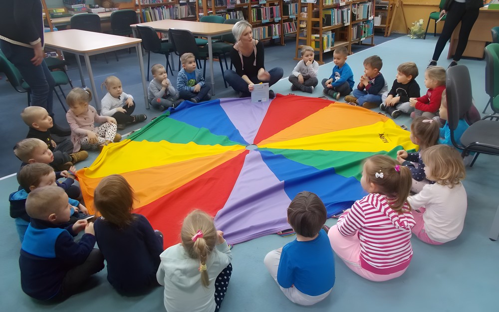 dzieci siedzą na chuście animacyjnej i słuchają bibliotekarki