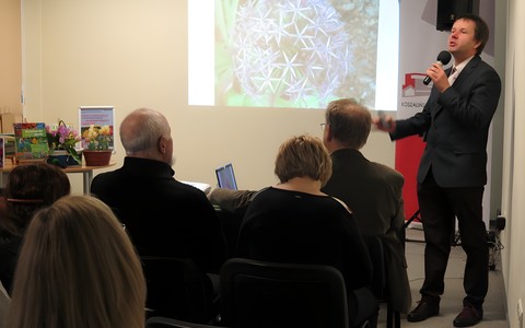 Paweł Kaźmierski podczas wykładu „Wiosenne rośliny cebulowe” stoi z prawej strony, na pierwszym planie widnieje zgromadzona publiczność