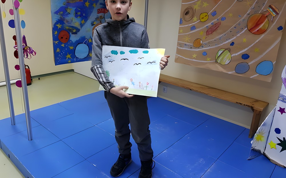 Chłopiec prezentuje swoją pracę plastyczną.