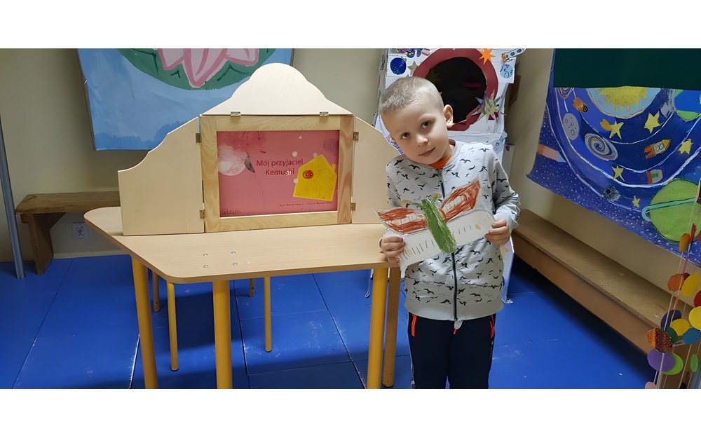 Chłopiec prezentuje swoją pracę plastyczną.