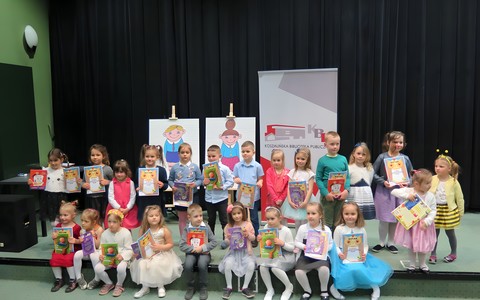 Przedszkolaki z Koszalina i powiatu koszalińskiego biorące udział w przeglądzie. Dzieci w pierwszym rzędzie siędzą, w drugim stoją. Wszyscy trzymają nagrody książkowe.