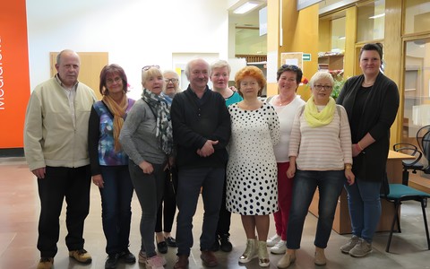 Senior i seniorki ze Stowarzyszenia VivaMY stoją na holu przy wypozyczalni w budynku głównym  KBP z pracownikami: Leszkiem Laskowskim oraz Anną Wieczorek.